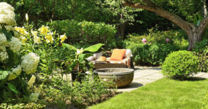 Decorative cast stone planter next to rattan sun loungers under old apple tree